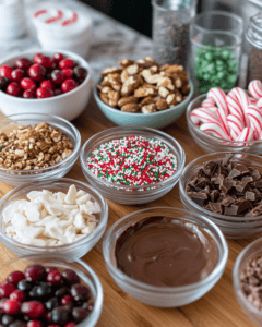 Bowls of ingredients for Christmas bark, including melted chocolate, candy canes, nuts, and sprinkles, arranged on a wooden countertop.