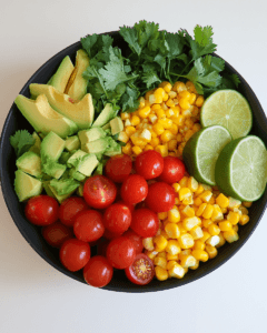 Bowl of corn salad with avocado and lime wedges.
